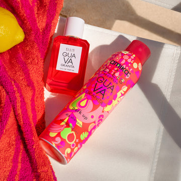 GUAVA GRANITA Eau de Parfum 50ml and Amika x Ellis Brooklyn GUAVA GRANITA Perk Up Dry Shampoo on white beach chair next to pink and orange beach towel and a lemon on a background of tan sand