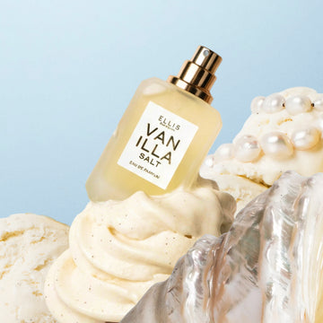 Eau de parfum VANILLA SALT (7,5 ml, sans capuchon), placée derrière une coquille argentée sur une glace à la vanille garnie de perles, le tout sur fond bleu.