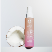 Brume parfumée pour cheveux et corps Sand 50ml sur une table blanche à côté d'une noix de coco, sur fond blanc.