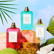 GUAVA GRANITA 50ml Eau de Parfum, MIAMI NECTAR 50ml Eau de Parfum and  ISLA SIRENA 50ml Eau de Parfum without caps covered in water droplets sitting on sliced guavas, sliced pineapple, sliced coconuts, and green coconuts on blue background with green palm leaves
