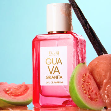 GUAVA GRANITA Eau de Parfum 50ml with a vanilla bean leaning against the cap sits on reflective surface between slices of cut guava all covered in water droplets on a blue background.