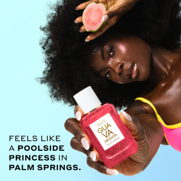Woman with brown hair wearing a pink and yellow bikini top holds GUAVA GRANITA Eau de Parfum 50ml covered in water droplets out in front of her in one hand and a slice of guava in her other hand next to her head against a blue background with black text that reads 