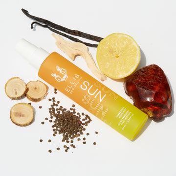 Sun Hair and Body Fragrance Mist 100ml on white background with vanilla bean, cedarwood, lemon, piece of amber, and seeds.