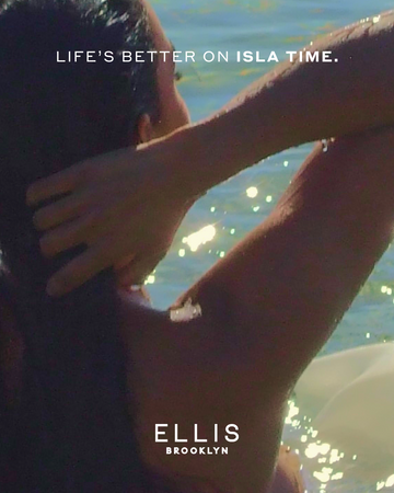 Closeup of woman with brown hair in the ocean, facing away with white text that reads "Life's better on isla time." and a white Ellis Brooklyn logo.