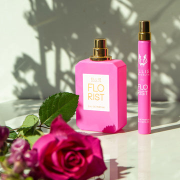 Florist 50ml Eau De Parfum with cap removed on white table next to Florist 10ml Eau De Parfum Travel spray behind pink roses, against white background with shadows.
