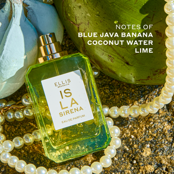 ISLA SIRENA Eau de Parfum 50ml without cap lays on top of a white string of pearls, and against a bunch of blue bananas and a green coconut with white text that reads 
