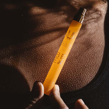 Modèle aux cheveux noirs portant un débardeur noir, tenant le spray de voyage Bee 10ml Eau de Parfum avec le capuchon enlevé contre sa poitrine.