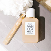 Vanilla Milk 50ml Eau de Parfum et Vanilla Milk 10ml Eau de Parfum Travel Spray sur un livre gris à côté d'une fleur blanche.