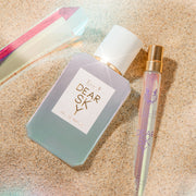 Dear Sky 50ml Eau De Parfum and Dear Sky 10ml Eau De Parfum Travel Spray slightly buried in sand next to a crystal.