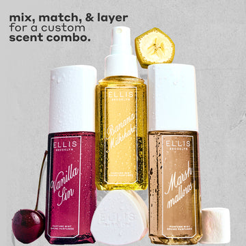 VANILLA SIN Perfume Mist 240ml next to a cherry, BANANA Milkshake Perfume Mist 240ml sitting on top of its cap, MARSHMALLOWS Perfume Mist 240ml with a slice on banana on top of it and a marshmallow next to it, all covered in water droplets on a gray, rough background with black text that reads 