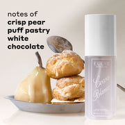 COCOA BLANCO 90 mL perfume mist bottle next to a pear, choux pastry, and spoon in a silver plate on a light beige background with text reading 'notes of crisp pear, puff pastry, white chocolate'.