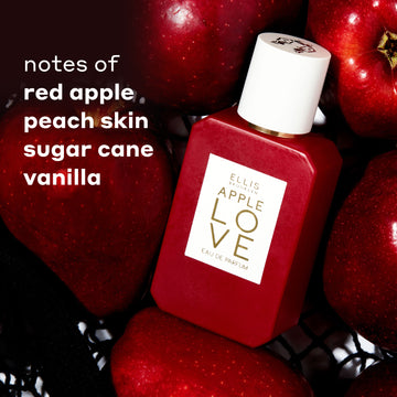 APPLE LOVE Eau de Parfum 50 mL bottle in red with a white cap, surrounded by fresh red apples. Text on the left reads 