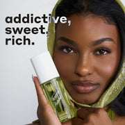 Woman with black hair wearing a green scarf on her head and holding a bottle of FOREVER PISTACHIO Perfume Mist 90ml against her cheek on a white background with black and white text that reads 