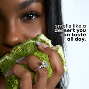 Woman with black hair wearing a diamond ring and holding green cake with white icing against a white background with black and gray text that reads 