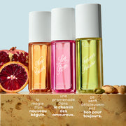 Brume de parfum NEW CRUSH 90ml, Brume de parfum LOVE POM 90ml et Brume de parfum FOREVER PISTACHIO 90ml sur du marbre beige entre des tranches de grenade, d’orange sanguine et des pistaches, sur un fond bleu clair avec un texte blanc qui dit « la magie d’un nouveau béguin. Une promenade dans le chemin des amoureux. Ca sent délicieusem bon pour toujours. »
