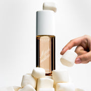 Brume Parfumée MARSHMALLOWS 240 ml avec une guimauve posée sur le bouchon, posée sur une pile de guimauves et une main attrapant une guimauve dans la pile sur un fond blanc