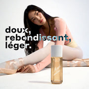 Modèle aux cheveux bruns portant un haut rose, un justaucorps jaune, des collants blancs et des chaussons de ballet roses, assise et s'étirant vers l'avant avec un flacon de MARSHMALLOWS Perfume Mist 240 ml posé sur le sol blanc devant elle, sur un fond blanc avec du texte blanc, noir et bleu indiquant « doux, rebondissant, leger ».