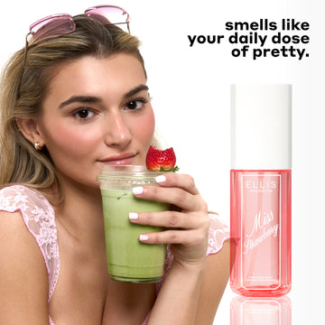 Woman with blonde hair wearing a pink lace tank top, gold hoop earrings, and pink sunglasses on her head holds a clear plastic cup of matcha tea with a half eaten strawberry on top of it next to MISS STRAWBERRY Perfume Mist 90ml with black text that reads 