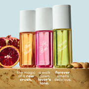 NEW CRUSH Perfume Mist 90ml, LOVE POM Perfume Mist 90ml, and FOREVER PISTACHIO Perfume Mist 90ml on tan marble between sliced pomegranate, blood orange, and pistachios against a light blue background with white text that reads 
