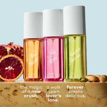 NEW CRUSH Perfume Mist 90ml, LOVE POM Perfume Mist 90ml, and FOREVER PISTACHIO Perfume Mist 90ml on tan marble between sliced pomegranate, blood orange, and pistachios against a light blue background with white text that reads 