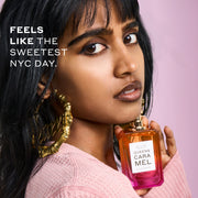 Woman with black hair wearing a pink sweater and gold hoop earrings that say 