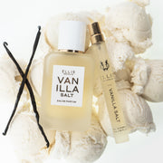 Vanilla beans, Vanilla Salt 50ml Eau De Parfum, and Vanilla Salt 10ml Eau De Parfum Travel Spray resting on scoops of vanilla ice cream, on white background.