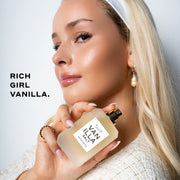 Model with blond hair and nude nail polish wearing white headband, pearl earring, gold rings, and cream boucle shirt holding Vanilla Salt 50ml Eau De Parfum without cap near shoulder on white background with black text that reads 
