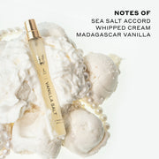 Vanilla Salt 10ml Eau De Parfum Travel Spray resting on whipped cream, vanilla ice cream, and pearl necklace, on white background next to black text that reads 