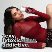 Model with brown hair wearing gold earrings, a red mesh shirt, and black sequined shorts lays down propped up on her arm while holding VANILLA SIN 240ml perfume mist on a white background with black, white, and blue text that reads 