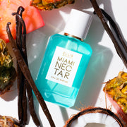 Le parfum MIAMI NECTAR Eau de Parfum 50ml est posé à côté de tranches d'ananas rose, d'une noix de coco coupée et de gousses de vanille sur un fond blanc