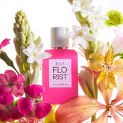 Eau de parfum Florist 50 ml sur fond blanc entouré de fleurs roses, blanches, jaunes et orange.