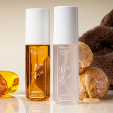 MISS AMBER and COCOA BLANCO 90ml Perfume Mist bottles displayed side by side with cream-filled pastries, a brown faux fur jacket, and amber. 