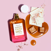 Queens Caramel 50ml Eau De Parfum with cap removed, and melted caramel, caramel squares, pieces of white chocolate, and pink salt, on light pink background.