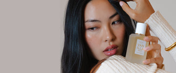 Model with brown hair and nude nail polish wearing white sweater and gold bracelet holding Vanilla Salt 50ml Eau De Parfum on shoulder in one hand.