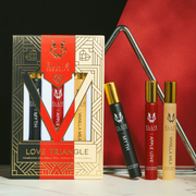 Black, red, beige and gold Love Triangle Fragrance Rollerball Trio Box showing Myth 10ml Fragrance Rollerball, Apple Love 10ml Fragrance Rollerball, and Vanilla Milk 10ml Fragrance Rollerball, and metal triangle on black and white marble table, on black and red background.