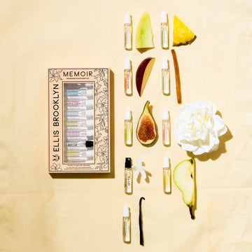 Memoir Fragrance Discovery Set box with beige and black floral design next to Dear Sky 1.5ml Vial, Miami Nectar 1.5ml Vial, Apple Love 1.5ml Vial, Salt 1.5ml Vial, Sun Fruit 1.5ml Vial, Florist 1.5ml Vial, Myth 1.5ml Vial, Sweet 1.5ml Vial, and Vanilla Milk 1.5ml Vial, on yellow background with fig, white flower, honeydew, vanilla bean, sandalwood, pineapple, and apple.