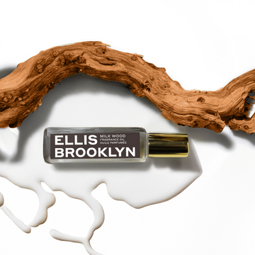 Milk Wood Fragrance Oil 15ml resting in milk next to piece of wood on white background. | english_image