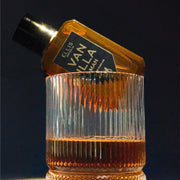 Vanilla Man 50ml Eau de Parfum posé sur le bord d'un verre de whisky, sur un fond noir.