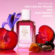 PLUM TONIC Eau de Parfum 50 ml à côté de prunes tranchées, de pierres d'ambre et d'un iris violet couvert de gouttes d'eau sur un fond rose avec du texte blanc indiquant 