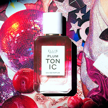 PLUM TONIC Eau de Parfum 50ml sur un collage de sequins roses, d'étoiles pailletées roses, d'une boule disco rose, de prunes, d'une femme portant une robe en sequins argentée et une pochette, de tissu rose et d'un collier en chaîne rose doré