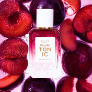 PLUM TONIC Eau de Parfum 50ml entouré de prunes tranchées, le tout sous l'eau avec des bulles sur un fond rose