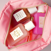 Pink Cosmetic Bag with gold zipper open and filled with QUEENS CARAMEL Eau de Parfum 50ml, FLORIST Eau de Parfum 50ml, VANILLA RICE Eau de Parfum 50ml, and GUAVA GRANITA Eau de Parfum 50ml on gray background