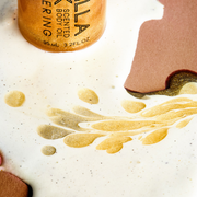 Vanilla Milk Shimmering Scented Body Oil 95ml poured onto melted vanilla ice cream  with cocoa powder, and gold glitter.
