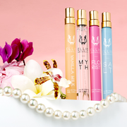 Vaporisateur de parfum voyage Vanille Lait 10ml Eau De Parfum, Myth 10ml Eau De Parfum Vaporisateur de Voyage, Florist 10ml Eau De Parfum Vaporisateur de Voyage et Sel 10ml Eau De Parfum Vaporisateur de Voyage sur une table blanche à côté de fleurs blanches, violettes, roses, blanches et jaunes, et d’un collier de perles, sur un fond rose clair.