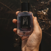 Model holding Sci Fi 50ml Eau De Parfum against brown backdrop.
