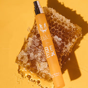 Spray de voyage Bee 10ml Eau de Parfum avec le bouchon retiré, reposant sur un morceau de rayon de miel, sur fond jaune.