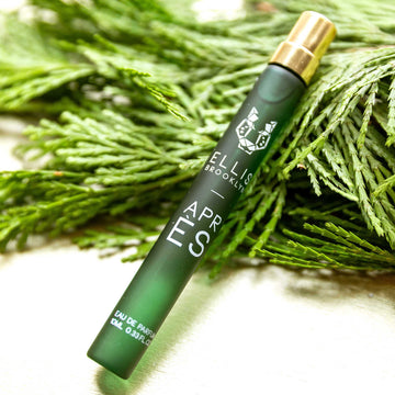 Apres 10ml Eau De Parfum Travel Spray resting on green pine leaves, on white fabric.