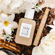 Vanilla Milk 50ml Eau De Parfum and Vanilla Milk Eau De Parfum Travel Spray on Cocoa Shells with assorted flowers, vanilla beans, and sandalwood.