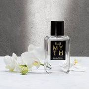 Myth 50ml Eau De Parfum on white table next to white flowers against grey wall.