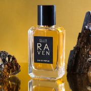 Raven 50ml Eau De Parfum on mirror, between two black crystals, on yellow background.